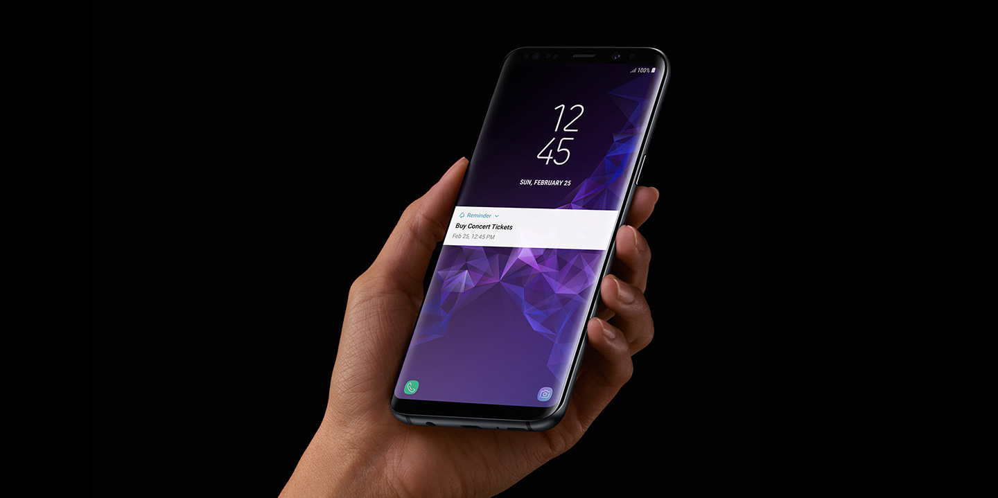 A person holding a Galaxy S9 Midnight Black with his left hand, receiving a ‘Buy concert tickets’ notification from Bixby Reminder