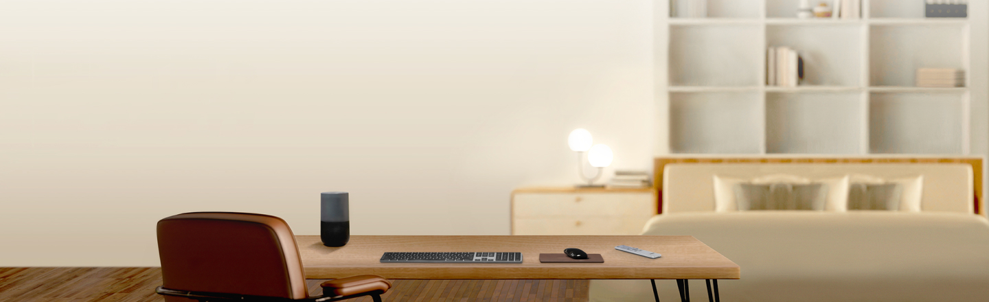 Um compartimento tem uma secretária e uma cadeira em pele em frente a uma cama e a uma estante. Na secretária está um monitor grande, um vaso com flores, uma coluna, um comando à distância e um rato e um teclado.