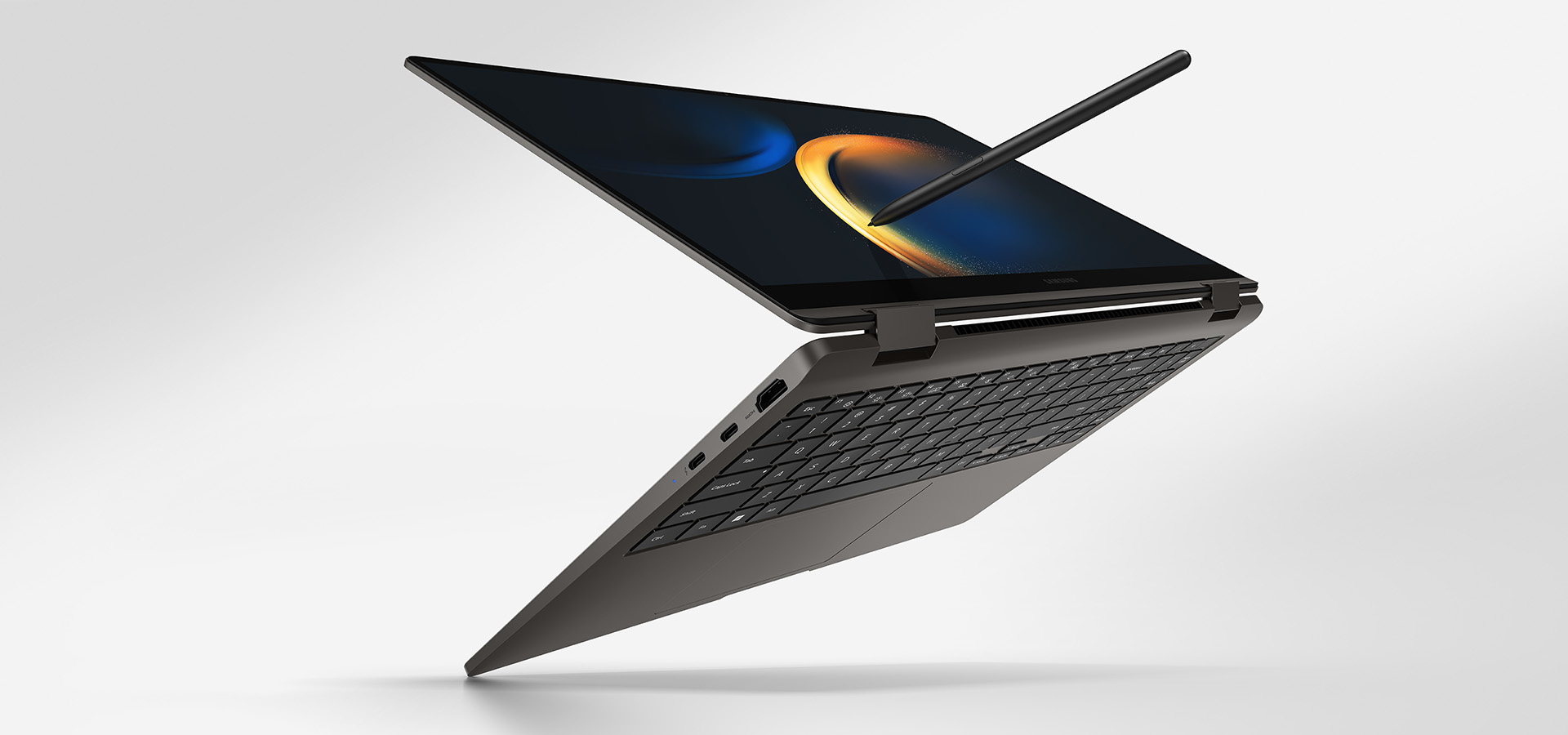 A graphite-colored Galaxy Book3 360 is folded slightly back, facing right with a black wallpaper onscreen and an S Pen touching the screen.