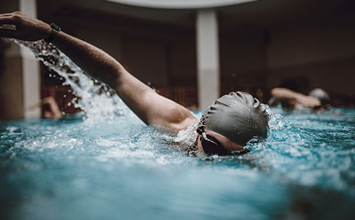 A person is swimming in a pool while wearing a Galaxy Watch4 Classic device.