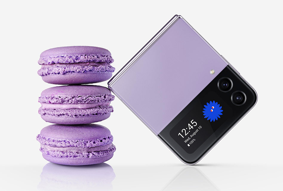 A folded Galaxy Z Flip4 in Bora Purple seen from the Cover Screen. It leans against a stack of three macarons of the same color. The folded device is similar in size to three stacked macarons.