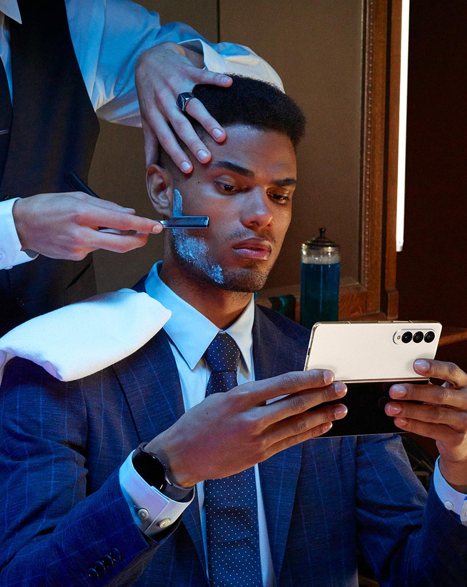 A man holds Galaxy Z Fold4, unfolded while sitting in a barber's chair.