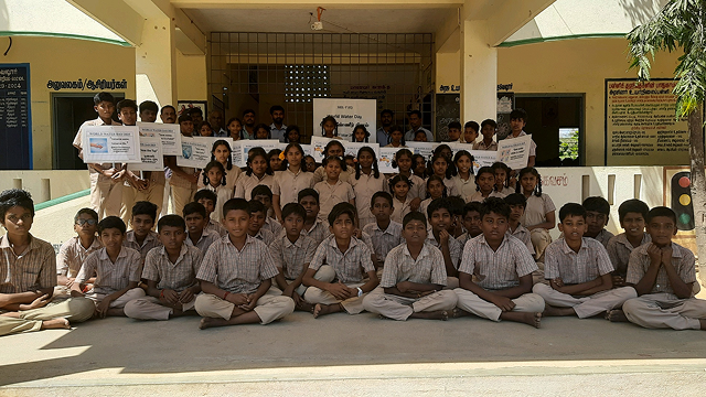 As part of a water replenishment program, students hold signs with related messages and pose for a group photo in front of a classroom in celebration of World Water Day.