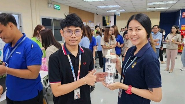 A Samsung Electronics employee hands a clear tumbler to a participant as part of a water-saving campaign, pausing to pose for a commemorative photo.