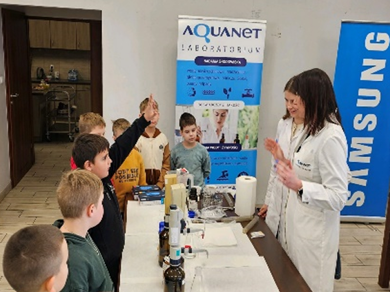 As part of a water replenishment program, researchers lead a hands-on water quality education session with children, one of whom is raising a hand to ask a question.