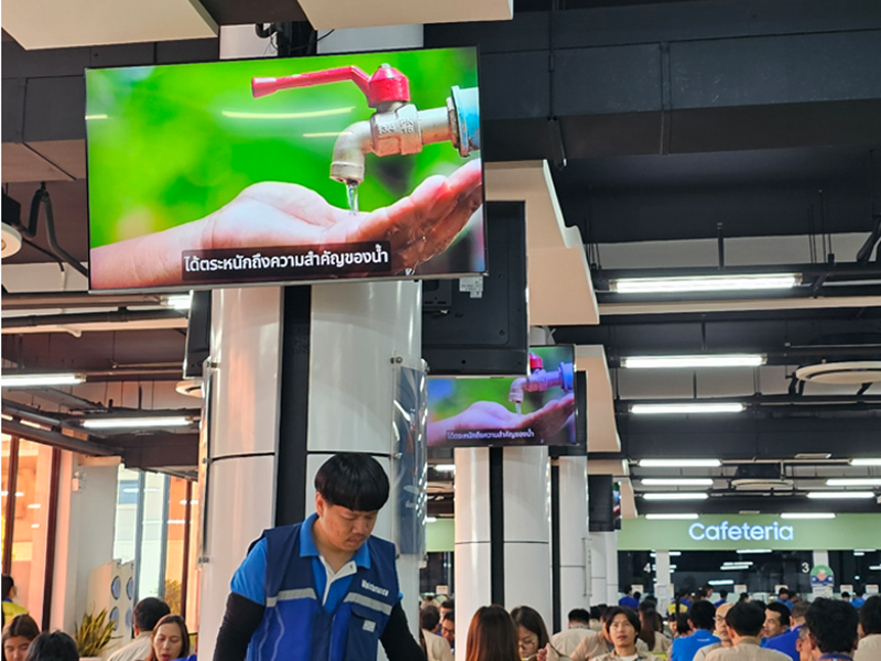 A water-saving campaign image emphasizing the importance of water is displayed on monitors inside a company cafeteria.